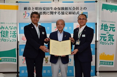 写真:協定書を持つ蕨市長と明治安田生命関係者